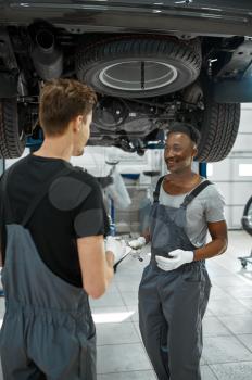 Two male mechanics looking on checklist, car service. Vehicle repairing garage, men in uniform, automobile station interior on background. Professional auto diagnostic