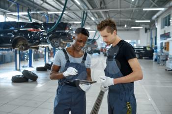Two male mechanics talking in car service. Vehicle repairing garage, men in uniform, automobile station interior on background. Professional auto diagnostics