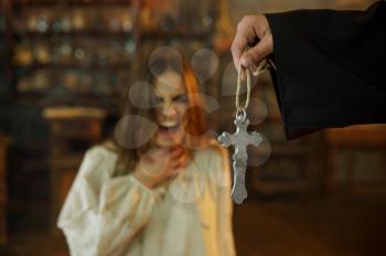 Male exorcist in black hood casting out devil from scary woman. Exorcism, mystery paranormal ritual, dark religion, night horror, potions on shelf on background