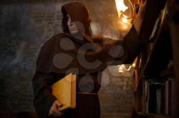 Male exorcist in black hood holding a torch. Exorcism, mystery paranormal ritual, dark religion, night horror, potions on shelf on background