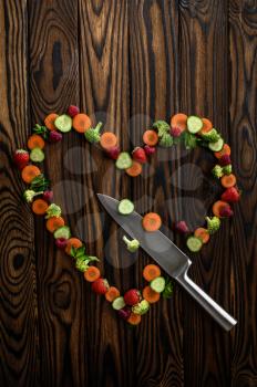 Vegetable heart with knife on wooden background, top view. Organic vegetarian food, grocery assortment, natural eco products, healthy lifestyle concept