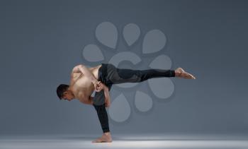 Male yoga keeps balanc in a difficult pose on one leg, grey background. Strong man doing yogi exercise, asana training, top concentration, healthy lifestyle