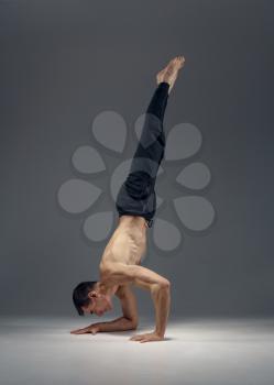 Male yoga keeps balanc on hands, meditation position, grey background. Strong man doing yogi exercise, asana training, top concentration, healthy lifestyle