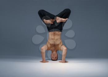 Male yoga stands on his head, hands and legs, meditation, grey background. Strong man doing yogi exercise, asana training, top concentration, healthy lifestyle