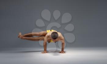 Muscular yoga stands on hands in difficult pose, meditation position, grey background. Strong man doing yogi exercise, asana training