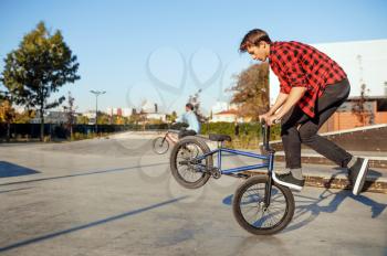 Two male bmx bikers doing tricks in skatepark. Extreme bicycle sport, dangerous cycle exercise, street riding, biking in summer park