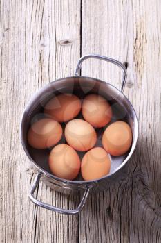 Brown eggs in water in a pan