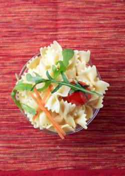 Bowl of bowtie pasta garnished with arugula and tomato