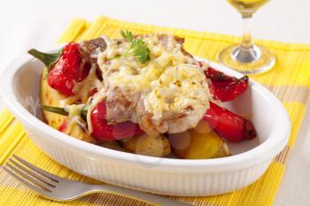 Pork chop with potatoes and red peppers topped with grated cheese 