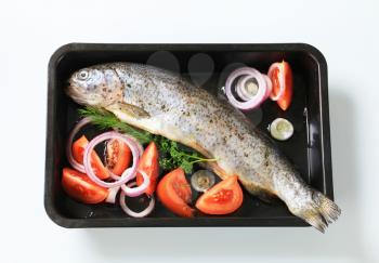 Fresh herb-stuffed trout and vegetable in a baking tin
