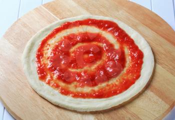 Tomato puree spread on raw pizza dough 