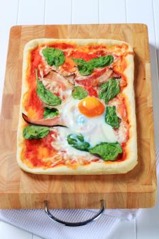 Pizza with prosciutto, spinach leaves and oven-roasted egg on top