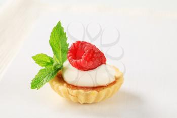 Creme brulee tartlet topped with cream and raspberry