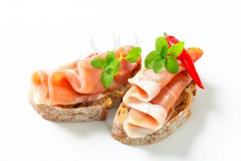 Prosciutto open faced sandwiches garnished with red chili peppers