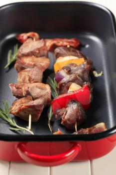 Shish kebabs and rashers of bacon in a roasting pan
