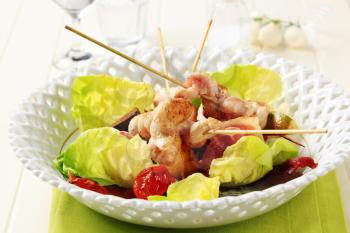 Chicken skewers and bacon strips served on lettuce leaves