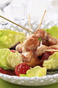 Chicken skewers and bacon strips served on lettuce leaves