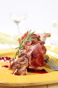 Meat skewer and crispy bacon strip garnished with cranberry sauce
