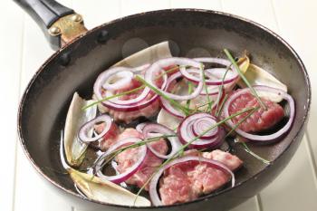 Raw pork, onion, and endive leaves on a frying pan