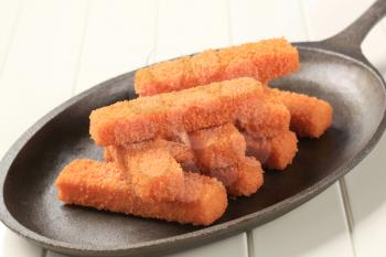 Stack of breaded fish fingers on a pan