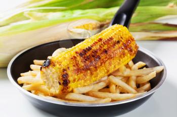 Grilled corn and French fries on a frying pan