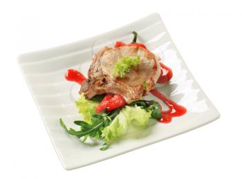 Roast pork chop and red pepper garnished with salad greens