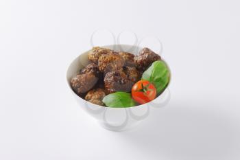 bowl of pan fried meatballs, cherry tomato and basil on white background