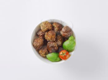 bowl of pan fried meatballs, cherry tomato and basil on white background