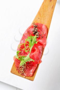 Thin slices of raw beef on wooden spatula