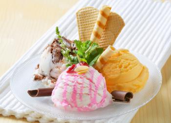 Three scoops of ice cream garnished with wafers and herbs