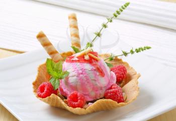Scoop of ice cream in wafer  bowl garnished with fresh raspberries and wafer sticks