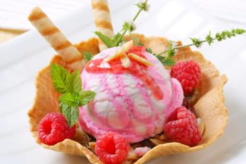 Scoop of ice cream in wafer  bowl garnished with fresh raspberries and wafer sticks