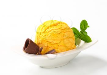Scoop of yellow ice cream garnished with chocolate curl