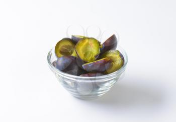 Halves of fresh ripe plums in glass bowl