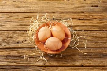 Three brown eggs on terracotta plate on wooden background