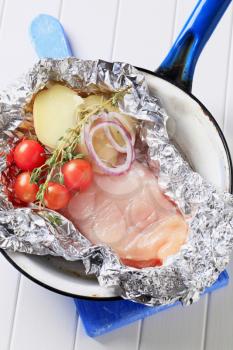 Raw chicken breast and vegetables in aluminum foil
