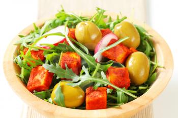 Salad greens with  green olives and diced paprika-coated cheese 