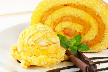Slice of Swiss roll with yellow ice cream and chocolate sauce