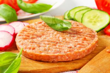 Raw burger patty and sliced vegetables on cutting board
