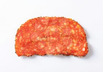 Single slice of black pepper-coated salami speckled with pieces of Comte cheese