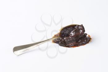 Spoon of plum jam on white background