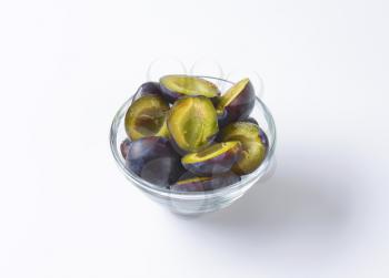 Halves of fresh ripe plums in glass bowl