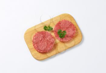 two raw hamburger patties on wooden cutting board
