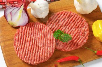 raw hamburger patties and vegetables on cutting board