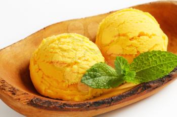 Two scoops of yellow ice-cream in olive wood bowl