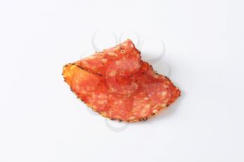 Thin slice of black pepper-coated salami speckled with pieces of Comte cheese