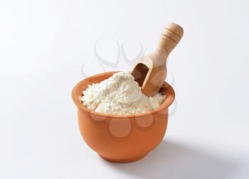 Finely ground flour and wooden scoop in terracotta bowl