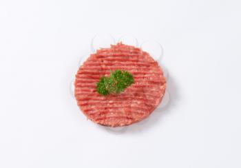 raw hamburger patty with parsley on white background