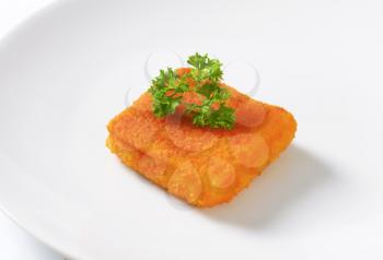 piece of fried fish with fresh parsley on white plate