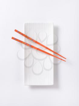 A pair of orange chopsticks on empty white sushi plate